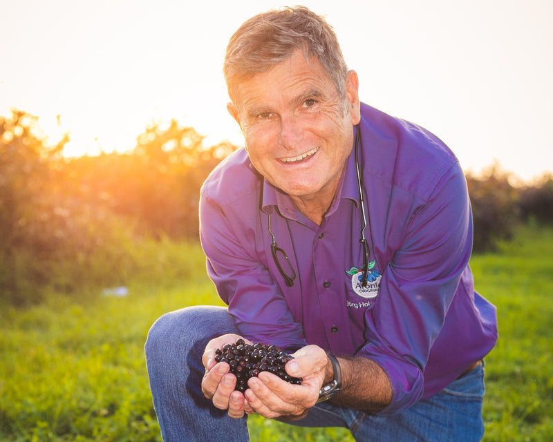 Jörg Holzmüller von Aronia ORIGINAL kniet auf einer Wiese im Abendlicht und hält eine Handvoll frisch geernteter Aroniabeeren