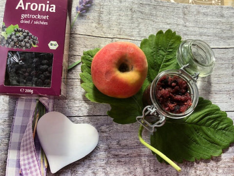 Apfel-Aronia-Chutney im Bügelglas neben getrockneten Aroniabeeren und frischem Obst