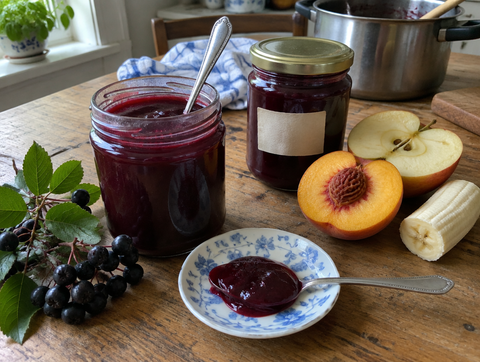Aronia-apple-banana-peach jelly in a jar, next to peach, apple, banana and aronia berries (symbolic image)