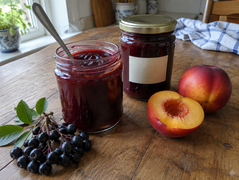 Aronia and nectarine jam in two jars, with nectarines and aronia berries (symbolic image)