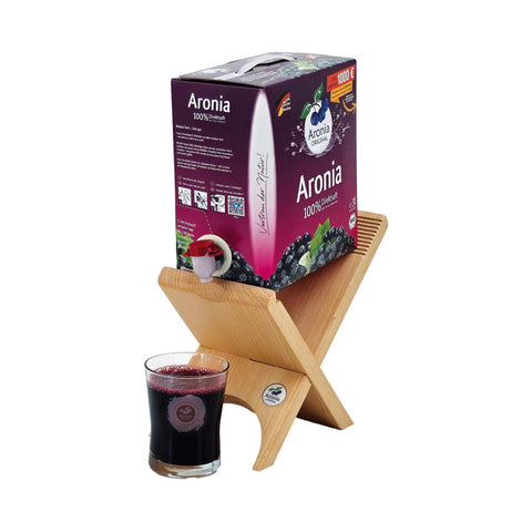 Aronia-Bag-in-Box auf Holzständer, daneben gefülltes Glas mit dunkelrotem Saft.