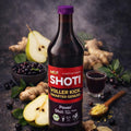 Dunkle SHOTI-Saftflasche mit violettem Deckel, daneben halbierte Birne, Ingwerknollen, Aroniabeeren und gefülltes Schnapsglas